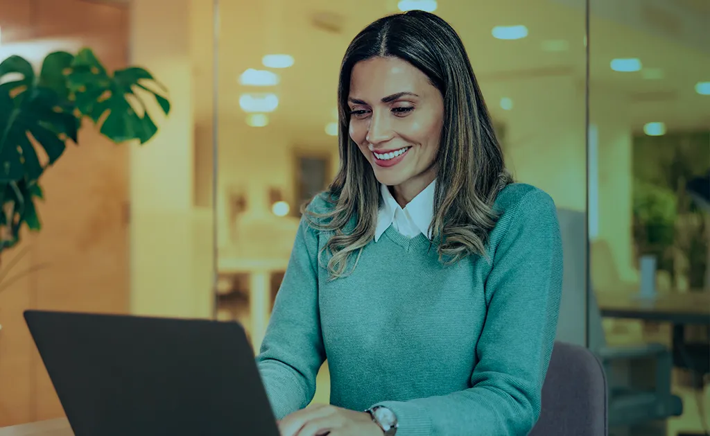 Mulher sorridente trabalhando em um laptop no escritório, executando a governança no RH.